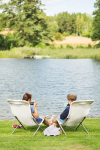 Rear view of couple having coffee on deck chairs at lake chairs