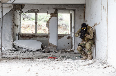 Man holding rifle while standing against wall