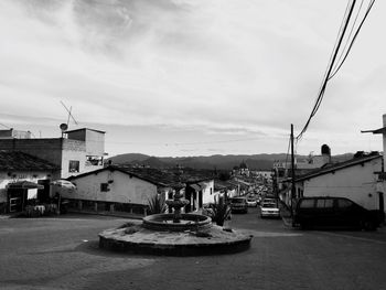 Fountain on street in city against sky