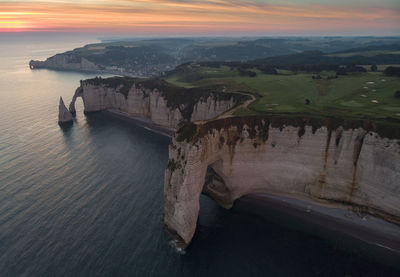 Aerial view of sea by rock formation against sky during sunset