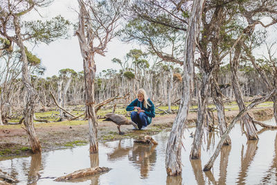 Man sitting by tree trunk against lake