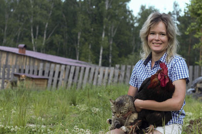 Portrait of young woman standing on field holding rooster