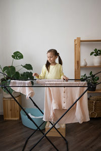 Small girl hanging clothes on drying rack at home