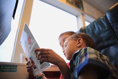 Low angle view of siblings reading brochure while sitting in boat