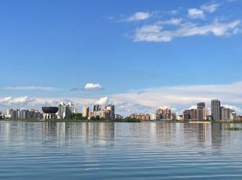 Sea by cityscape against blue sky