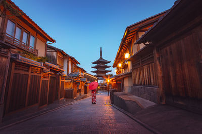 Illuminated street amidst buildings against sky in city