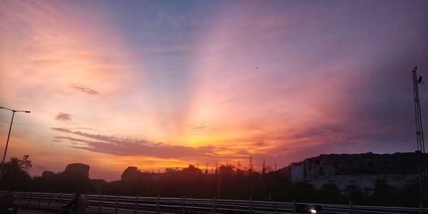 Silhouette buildings by street against sky during sunset
