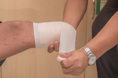 Cropped image of doctor wrapping bandage on leg in hospital