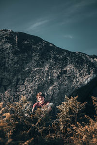 Man sitting on rock against sky