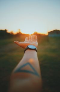 Cropped hand of man gesturing against sky during sunset