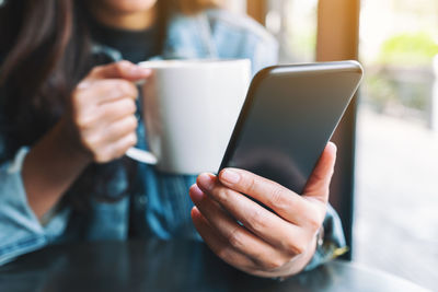 Midsection of businesswoman using smart phone while holding coffee cup at cafe