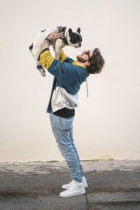 Side view of man carrying dog while standing at beach