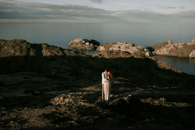 Woman standing on rock by sea against sky