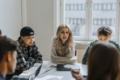 Young female student sitting with friends at desk in classroom