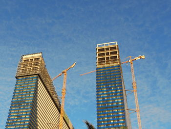 Low angle view of crane by building against sky