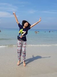 Woman with arms raised on beach against sky