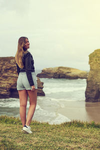 Rear view of young woman smiling while standing by sea against sky