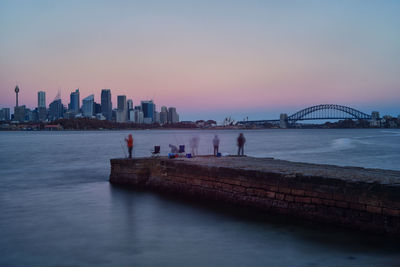 People fishing on pier against sydney harbor bridge