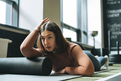 Young brunette woman doing stretching pilates on the massage roll in fitness club gym