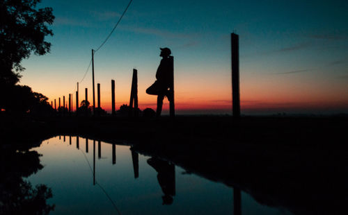 Silhouette man standing by lake against sky during sunset