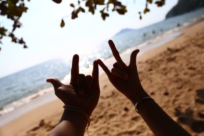 Cropped hands of couple showing rock sign at beach