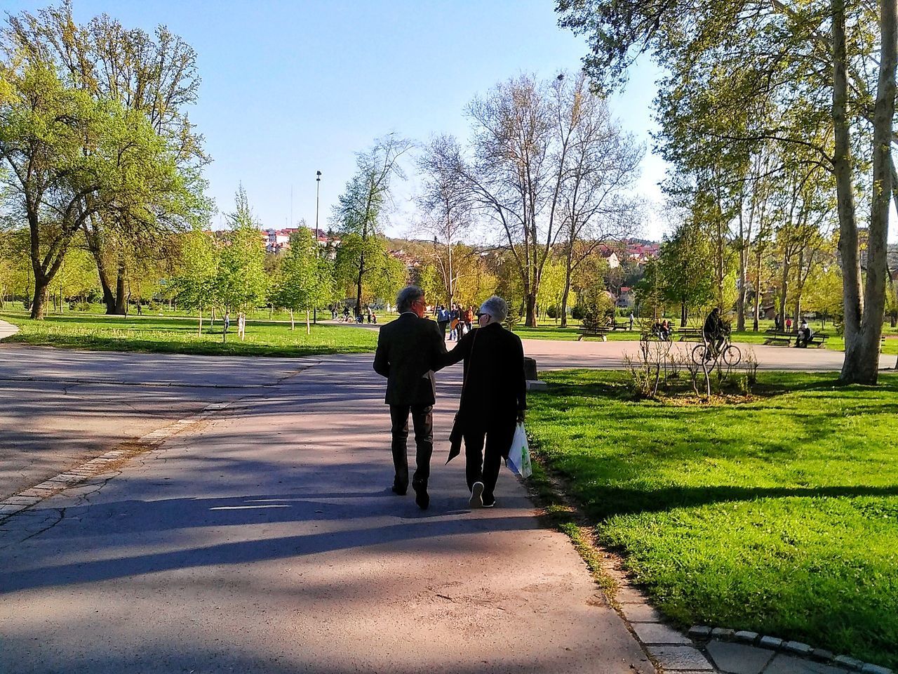 REAR VIEW OF PEOPLE WALKING ON FOOTPATH AT PARK