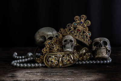 Close-up of human skulls and gold jewelry on table against black background