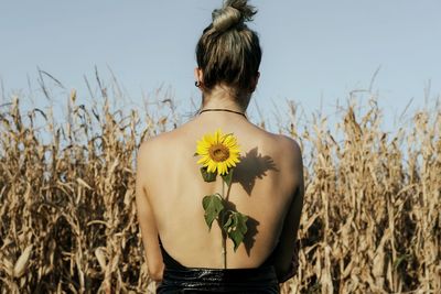 Rear view of woman with sunflower standing against plants on agricultural field