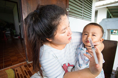 Mother inserting medicine to son through nose at home