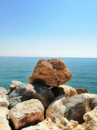 Rocks in sea against clear blue sky