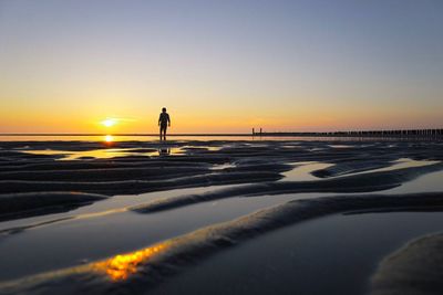 Silhouette person walking on beach against clear sky during sunset