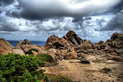 Rock formations by sea against cloudy sky