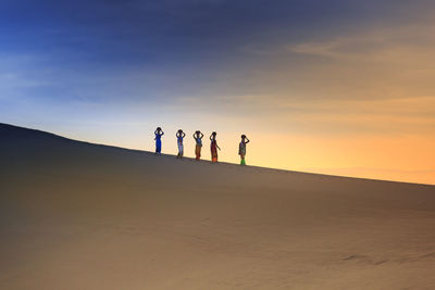 People on beach against sky during sunset