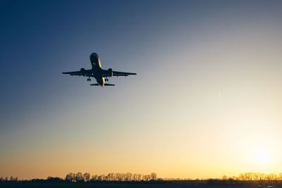 Low angle view of airplane flying against sky during sunset