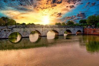 Arch bridge over river against sky during sunset