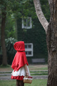 Side view of young woman standing by tree outdoors