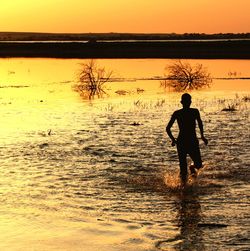 Silhouette man walking in lake against orange sky