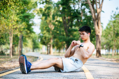 Side view of shirtless young man against trees