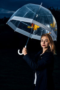 Portrait of young woman holding umbrella at night