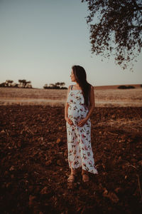 Pregnant woman standing on field against clear sky during sunset