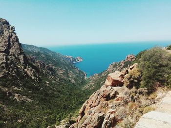 Scenic view of sea by mountains against clear blue sky