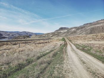 Dirt road amidst field against sky