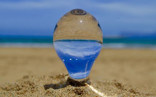Close-up of glass container at beach against sky
