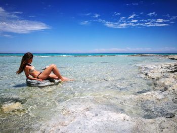 Side view of sensuous woman in bikini relaxing against sky at beach