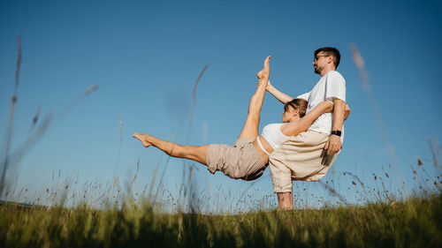 Man and woman dressed alike doing difficult pose while practicing yoga outdoors in the field