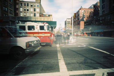 Cars on city street by buildings against sky