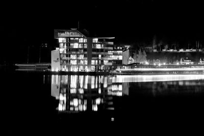 Illuminated buildings by lake against sky at night