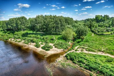 River by green field against blue sky on sunny day