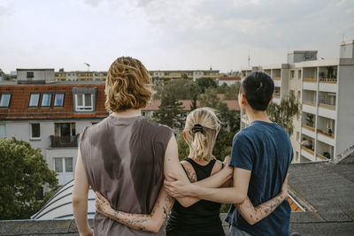 Rear view of male and female friends standing with arms around on rooftop