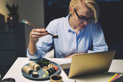 Businesswoman looking having food while working at desk in home office